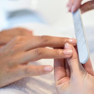 Close-up of a woman in a nail salon receiving a manicure by a beautician with. Beautician file nails to a customer.